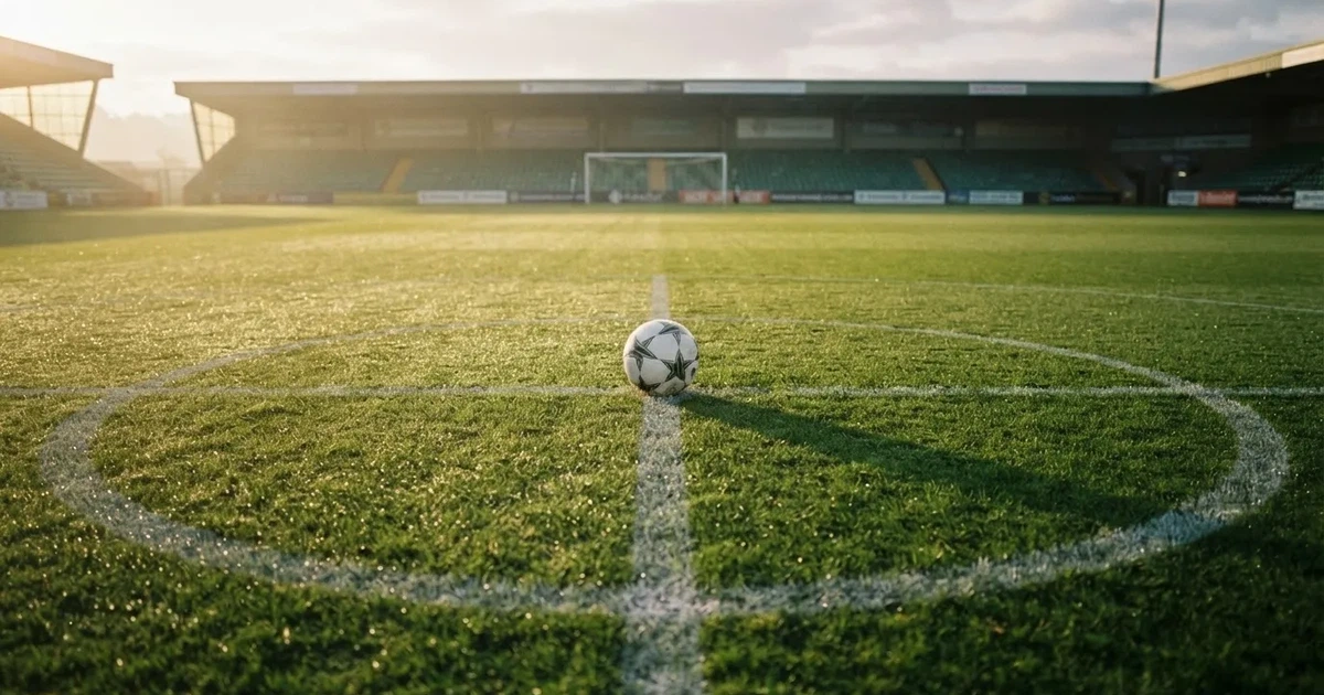 Een voetbal op de middenstip van een grasveld in het ochtendlicht