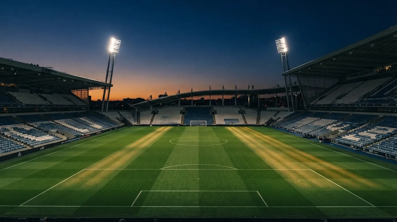 Een leeg voetbalstadion met lichtmasten bij schemering