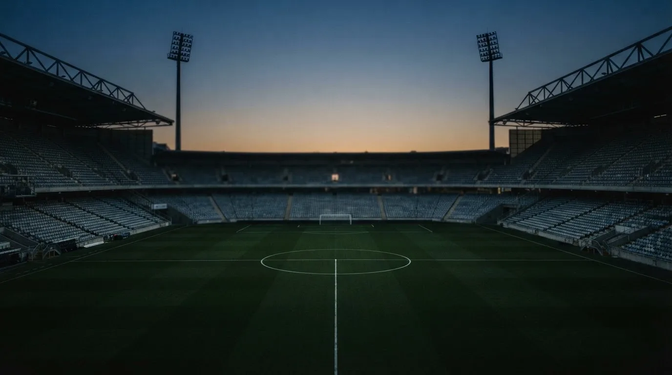 Een leeg voetbalstadion met lichtmasten bij schemering