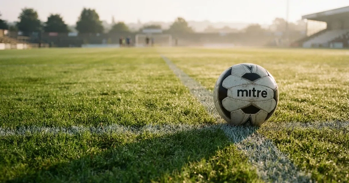 Een voetbal op de middenstip van een grasveld in het ochtendlicht