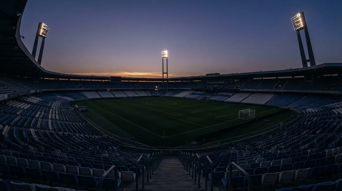 Een leeg voetbalstadion met lichtmasten bij schemering