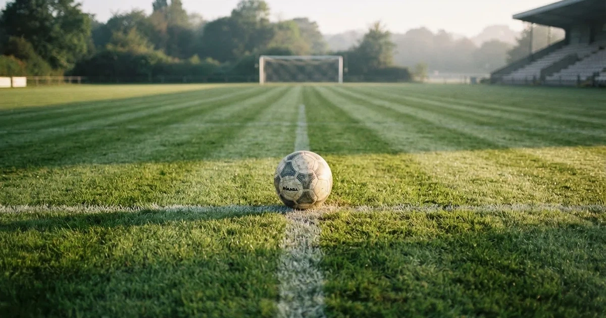 Een voetbal op de middenstip van een grasveld in het ochtendlicht