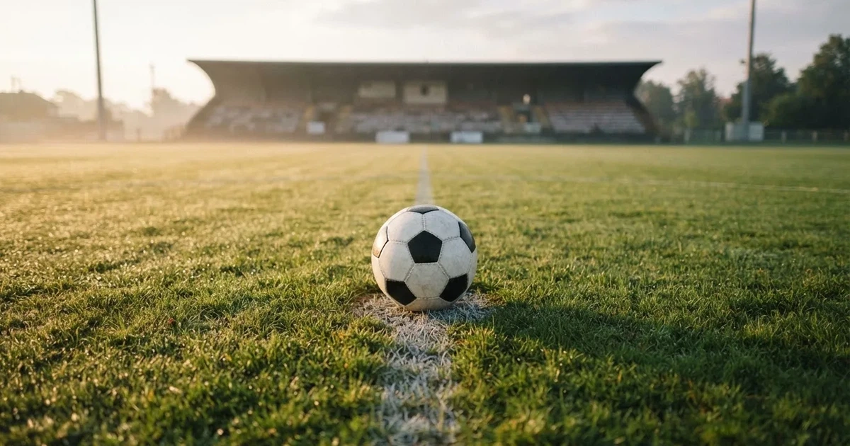 Een voetbal op de middenstip van een grasveld in het ochtendlicht