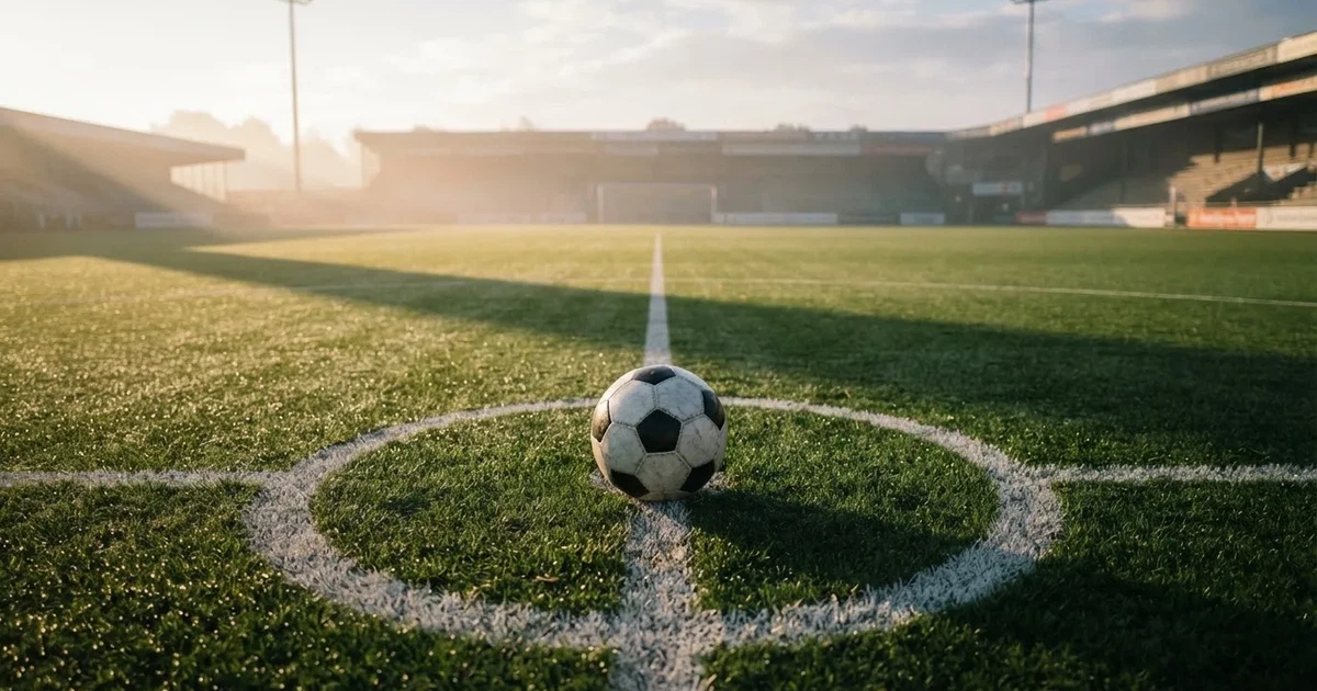 Een voetbal op de middenstip van een grasveld in het ochtendlicht