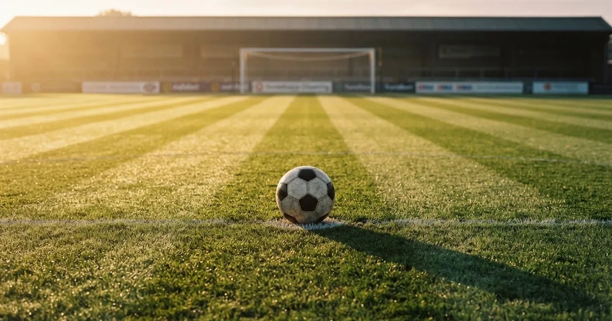 Een voetbal op de middenstip van een grasveld in het ochtendlicht