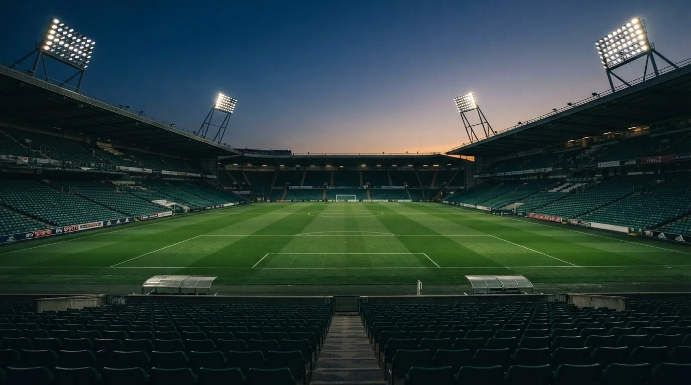 Een leeg voetbalstadion met lichtmasten bij schemering