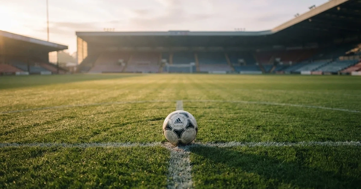Een voetbal op de middenstip van een grasveld in het ochtendlicht