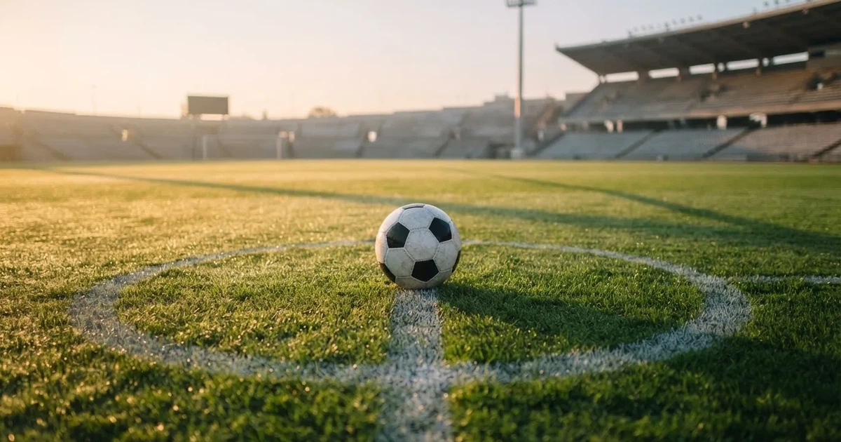 Een voetbal op de middenstip van een grasveld in het ochtendlicht